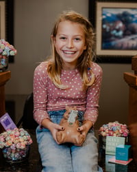 Blonde child in pink shirt holding a bear with cash on it.